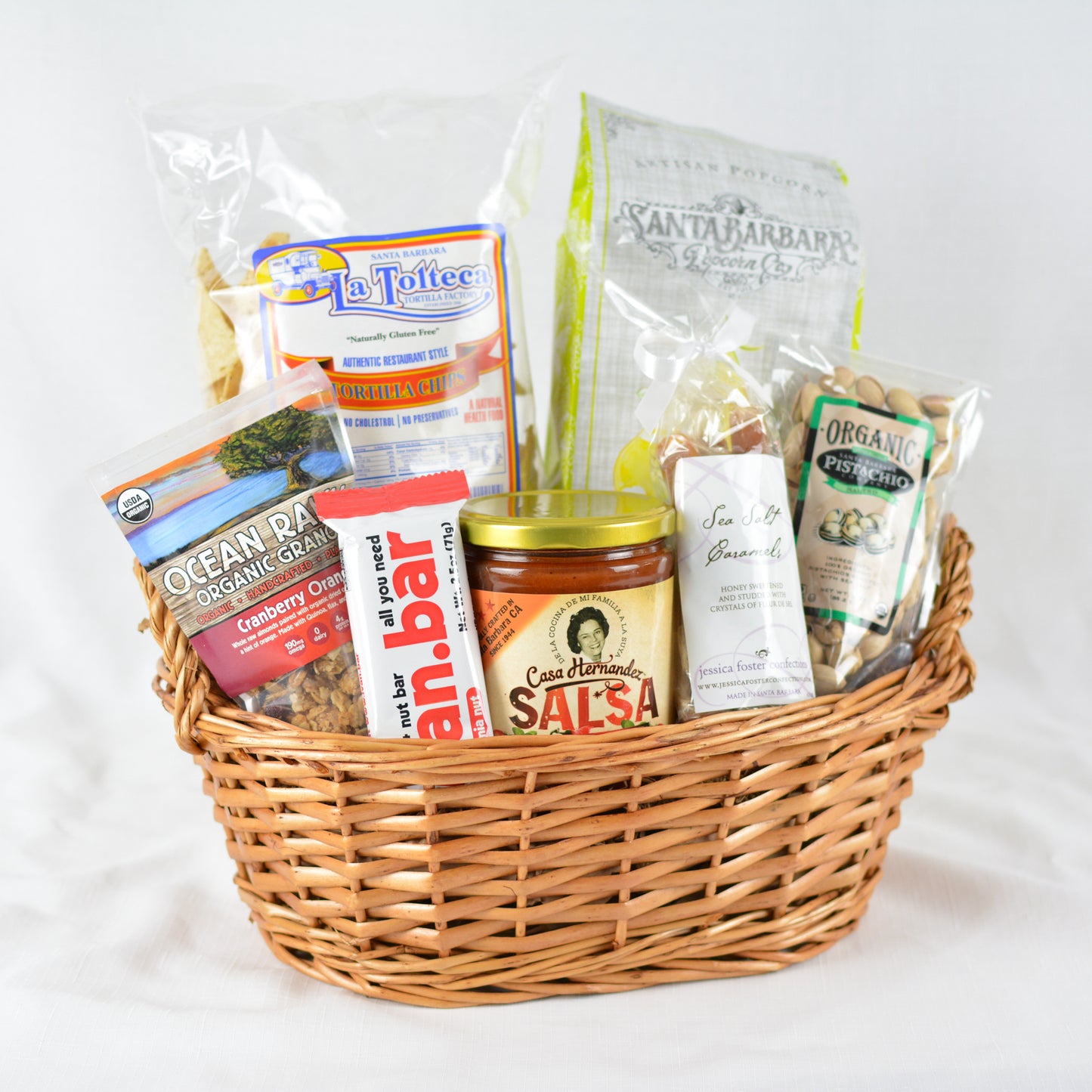 A gift basket filled with an assortment of gourmet snacks made in Santa Barbara, California including La Toltecca tortilla chips, Santa Barbara salsa, Santa Barbara pistachios, Santa Barbara popcorn, an Ivan protein bar, Jessica Foster handmade sea salt caramels, and Ocean Ranch organic granola.