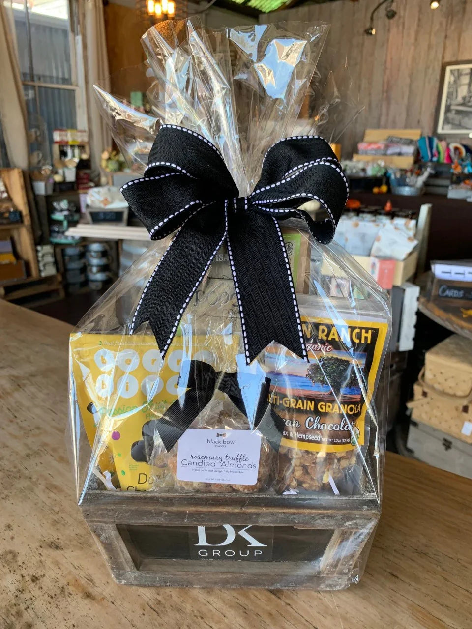 Gift basket with granola, candied almonds, and snacks wrapped in clear plastic with black bow