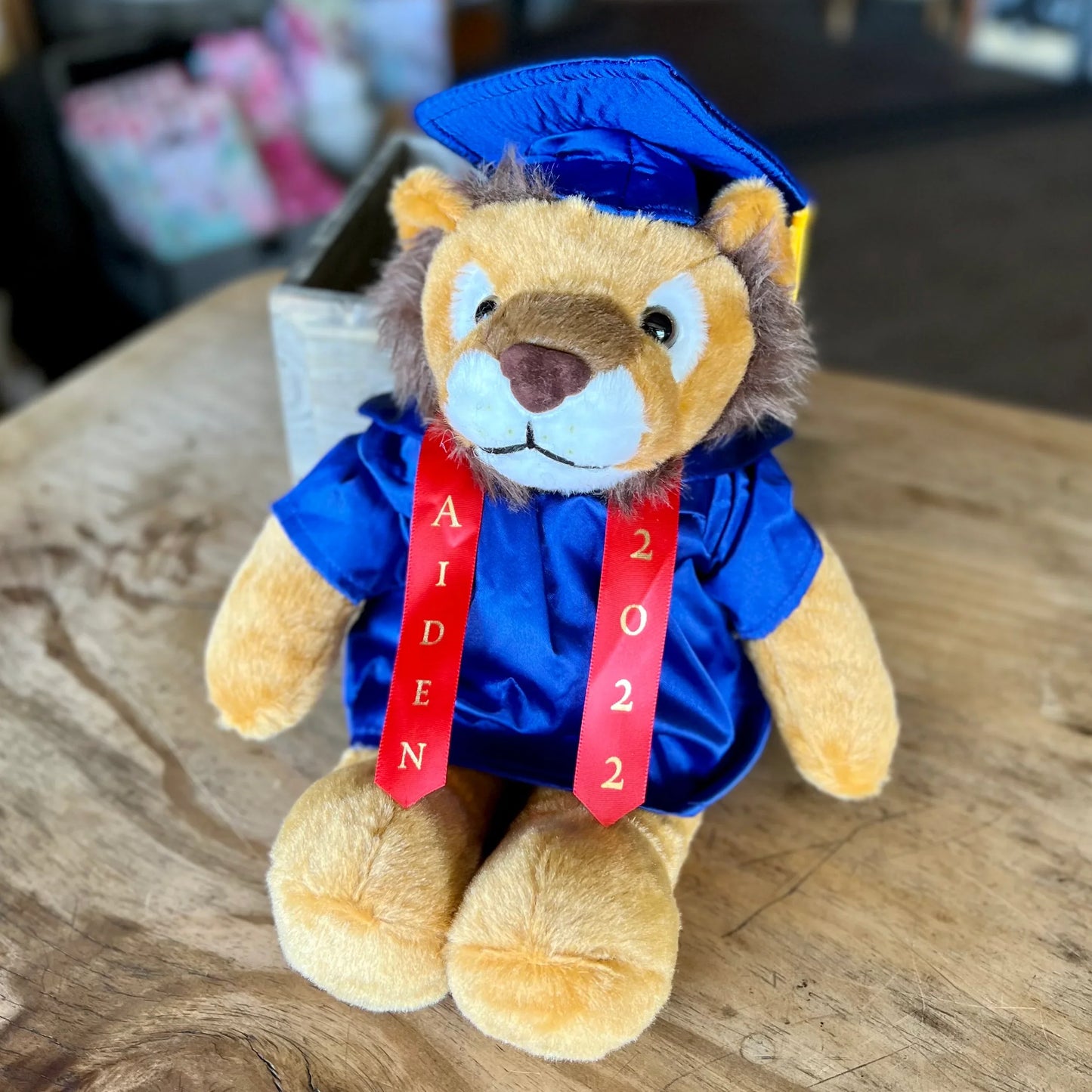 Graduation lion plush toy in blue cap and gown with red stole reading Aiden 2022