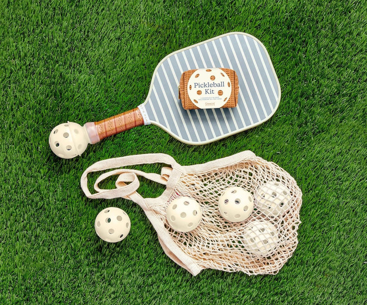 Pickleball paddle with striped surface, perforated balls, and net bag on green grass