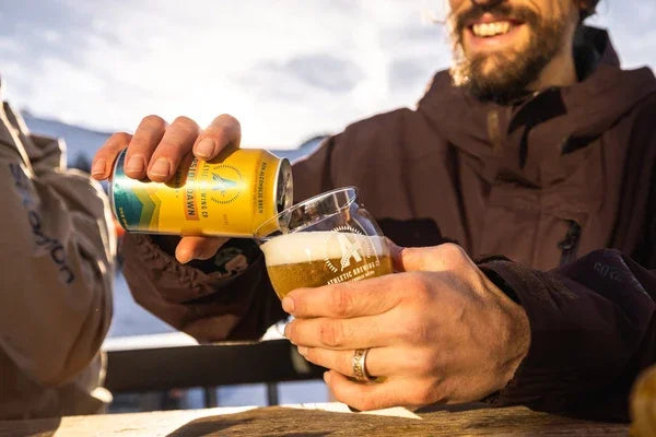 Man pouring yellow craft beer from can into glass outdoors, enjoying sunny day on balcony