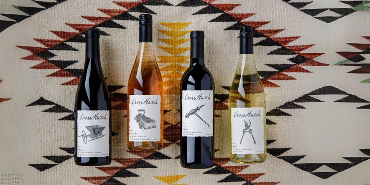 Four CrossHatch wine bottles with distinctive black and white labels on patterned textile background