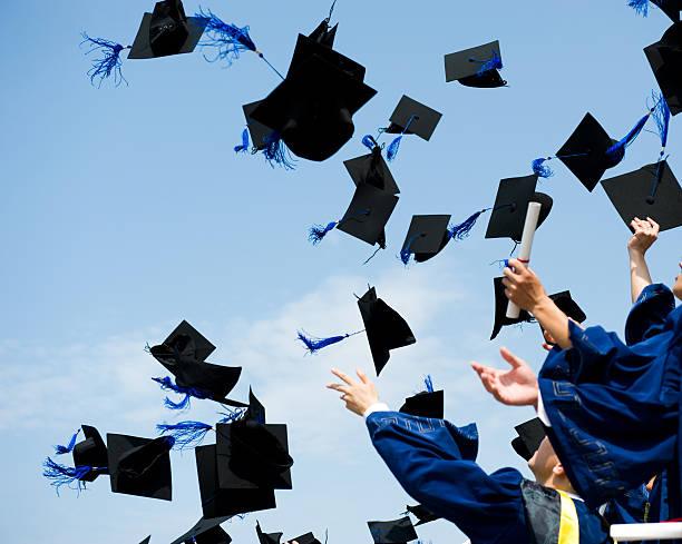 Graduates in blue gowns tossing black caps with blue tassels into the sky celebrating graduation